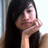 Pixelated close-up of a person with long dark hair holding hands near their face, wearing light-colored clothing against a bright background.