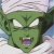 Green-skinned character with white eyes and purple mouth, pixelated static image showing facial features against light background.