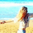 A woman with long blonde hair stands on a beach with arms outstretched, wearing a white top and blue jeans, against a backdrop of blue sky and ocean.