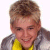 Pixelated close-up of a person with short light brown hair wearing a yellow shirt under a gray jacket against a white background.