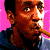 Pixelated image of a person with short dark hair wearing a blue shirt, holding a cigar in their mouth against a pink and cyan background with bold text.