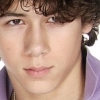 Close-up of a person with curly brown hair wearing a light purple shirt with white stripes, cropped to show only the upper chest and face.
