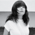 A grayscale pixelated image of a person with long dark hair wearing a white top against a light background.