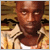 Pixelated static image of a person with brown skin tone wearing a light-colored shirt and dark jacket, set against a warm-toned background with horizontal stripes.