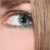 A close-up of a human eye with light skin tone, brown eyelashes, and visible eyebrow above it.