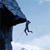 Pixelated static image of a dark blue climbing rope with a carabiner attached, hanging from the edge of a black rock face against a light blue sky background.