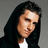 A person with long dark hair wearing a black hoodie over a white shirt appears in four -like against a gray background