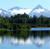 Pixelated landscape with blue sky, white clouds, green trees, and a body of water reflecting the scene.