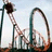 A roller coaster with orange and teal tracks against a light blue sky, viewed from multiple angles in an animated sequence.