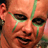 Pixelated close-up of a person's face with green streaks on cheeks, dark eyes, and visible mouth area.