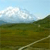Pixelated landscape with green fields, a light-colored path, and white clouds under a pale blue sky.