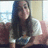 Pixelated static image of a person with long dark hair wearing a dark top, seated indoors with light-colored walls and a window in the background.