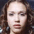 Pixelated close-up of a person with light skin, dark eyes, and long brown hair against a dark background.