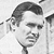 Black-and-white pixelated image of a person with short dark hair, wearing a light-colored shirt and dark tie, facing slightly right with a neutral expression.