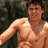A shirtless man with short brown hair stands against a dark background, smiling slightly; the word 'beautiful' appears in white pixelated text on his chest.