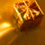 A golden gift box with a white ribbon and red bow sits on a reflective golden surface, viewed from a slightly angled perspective.