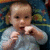 A child in a light blue shirt sits against a patterned blue background with green and yellow shapes, mouth open and hands near face.