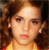 A pixelated close-up of a person with brown hair, wearing small earrings and a yellow garment with red accents.
