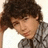 Pixelated image of a person with curly brown hair resting head on hand, wearing gray plaid shirt against light background; adjacent purple displays orange text 'nick jonas <3' in pixel font
