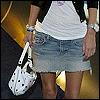 A person wearing a white t-shirt and light blue denim skirt holding a white polka-dot bag with black dots.