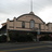 Static pixelated image of a building with a rounded roof and vertical spire, set against a light sky background.