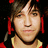 Pixelated close-up of a person with light skin, dark hair styled in two braids adorned with red ornaments, wearing a yellow garment against black background.