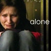 A person with dark hair sits with knees drawn up, wearing light blue jeans and a dark top with red accents, against a dimly lit background with the word 'alone' in white text.