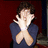 Pixelated image of a person with dark hair wearing a blue top, hands raised near face in front of red background.