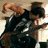A person in a black sleeveless shirt with white text plays a dark-colored electric guitar, transitioning from a standing pose to a seated position.