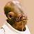 Pixelated static image of a character's head and shoulders with brown hair, visible facial features including an eye and mouth, wearing a white shirt against a beige background.