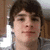 A pixelated image of a person with brown hair and light skin, wearing a gray shirt against a blurred indoor background.