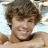 Pixelated static image of a person with brown curly hair, light skin tone, and visible facial features including eyes, nose, mouth, and chin.