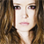 Pixelated close-up of a person with long brown hair, light skin tone, and pink lips against dark background.
