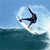 Pixelated static image of a person performing a surfing trick above ocean waves with water spray, set against a clear blue sky background.