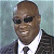 Pixelated image of a person wearing dark sunglasses, a white shirt, and a dark suit jacket with a tie, set against a light blue background.
