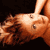 Pixelated static image of a person lying on their back with arms raised, featuring warm brown and orange tones against dark background.