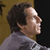Pixelated profile view of a person with dark curly hair wearing a gray shirt against a brown and black background.