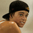 Pixelated image of a person wearing a black cap with a small yellow and red emblem on the right side, facing left.