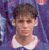 A pixelated portrait of a person with short brown hair wearing a white sleeveless top against a purple and blue gradient background.
