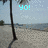 Pixelated beach scene with a vertical pole on the left, sandy shore, and water under a light blue sky, featuring cyan 'YO!' text in the upper center.