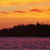 Pixelated sunset scene with orange and yellow sky, dark silhouette of landmass, and purple water below.