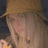 Static 48x48 pixel icon showing a close-up of a person with light brown hair wearing a wide-brimmed hat, partially visible face with pinkish skin tones and dark eyes, against a dark blue background.