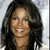 A pixelated close-up of a person with long dark hair, light skin, and a smiling expression against a light gray background.