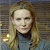 Pixelated portrait of a person with long light brown hair wearing a dark turtleneck under a light blue top against a blurred background with horizontal lines and two small yellow lights.