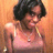 A person with short dark hair wears a light pink tank top and silver necklace against an orange background.