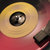 A pixelated close-up of a circular yellow object with a dark center and light reflections, set against a blurred red and black background.