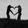 Two silhouetted figures stand on a grassy hilltop, their arms extended to form a heart shape with their hands against a light sky background.