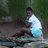 A pixelated image shows a person in a white shirt and blue shorts sitting on a rock near water, with greenery in the background and blue text reading "Pure as Wicked" on the right.