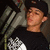 A person wearing a black cap and black shirt with white graphic design, positioned against a blurred background.