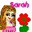Pixelated image of a girl with long brown hair wearing a pink dress, standing next to a red flower with green leaves, with pink text reading 'Sarah' above her head.
